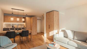 A modern living room with a sofa, a dining area with chairs and a table, and a kitchen with wooden cabinets and pendant lights.
