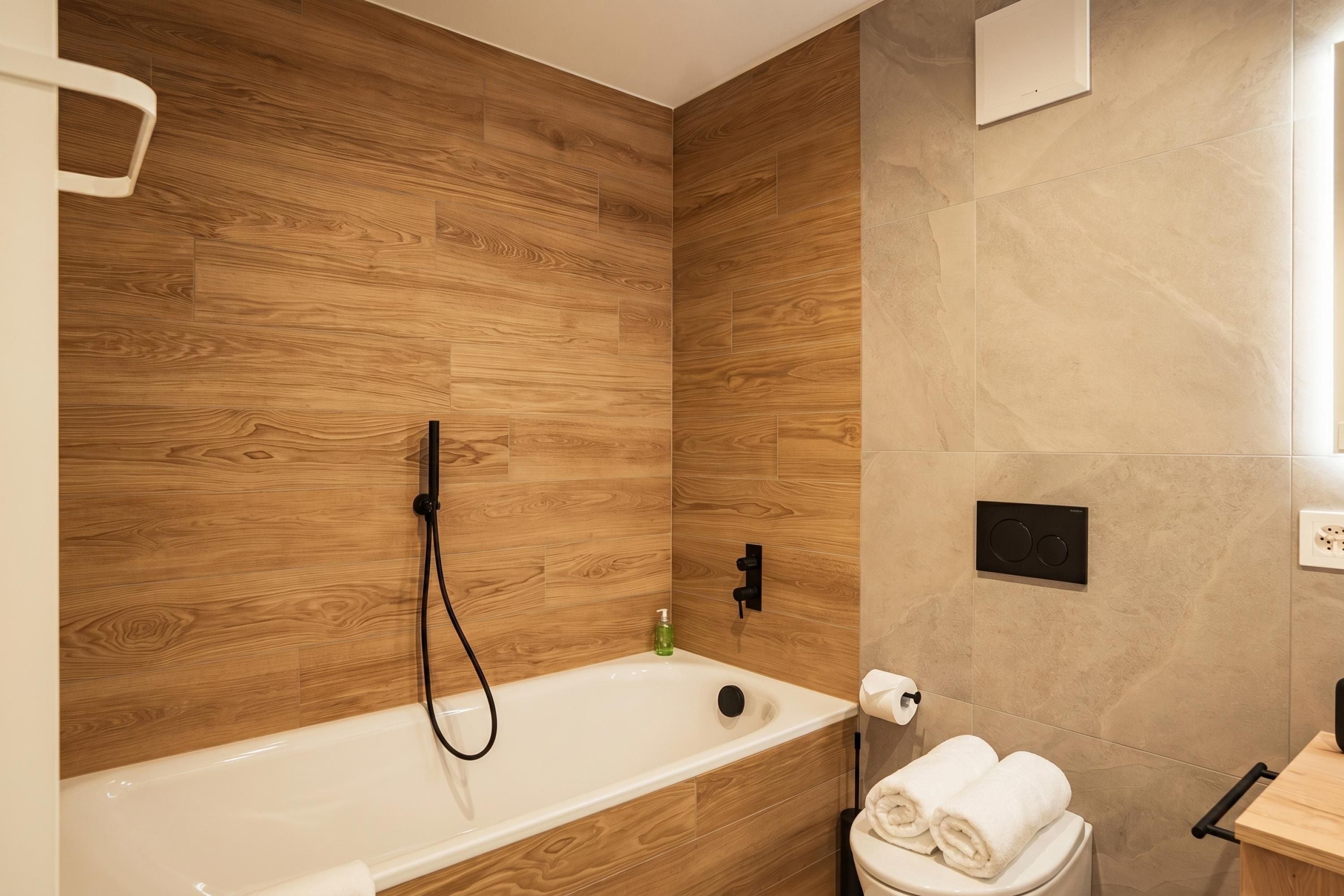 A modern bathroom with a wooden wall, a bathtub, a toilet, and a sink.