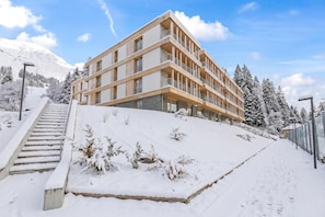 A multi-story hotel with a modern design, located on a snowy hillside with a staircase leading up to the entrance. - Residenza Castanea 005 San Bernardino Alpine Apartments, San Bernardino, Switzerland (San Bernardino)