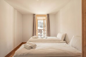 Un dormitorio con dos camas, una ventana con cortinas y vista a un paisaje nevado.