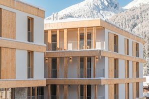 A multi-story building with balconies, wooden facade, and a mountainous backdrop.