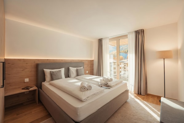A hotel room with a large bed, a nightstand, a lamp, and a view of a mountain landscape.