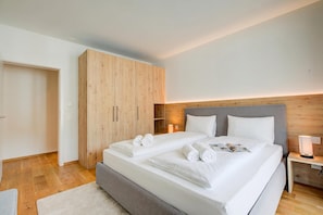 A modern bedroom with a double bed, wooden wardrobe, bedside table, and a nightstand with a lamp. - Residenza Castanea 003 San Bernardino Alpine Apartments, San Bernardino, Switzerland (San Bernardino)