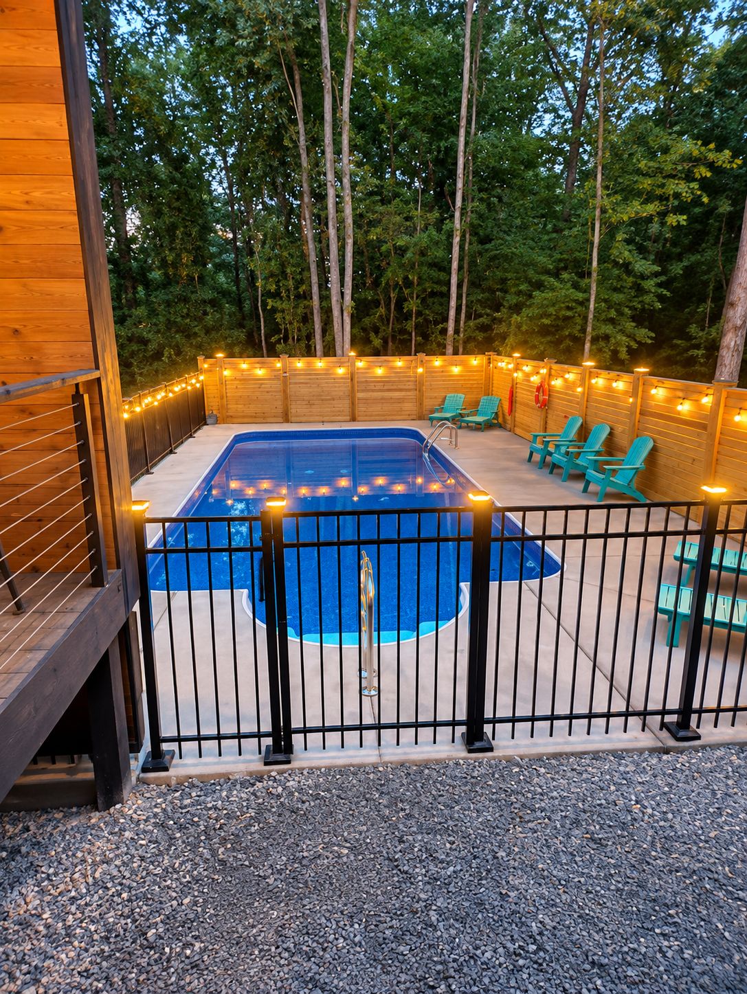 A swimming pool with a black fence, surrounded by wooden deck and chairs.