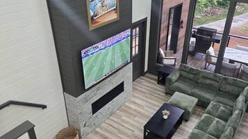Uma sala de estar moderna com televisão de tela plana, lareira e uma grande janela com vista para um jardim.