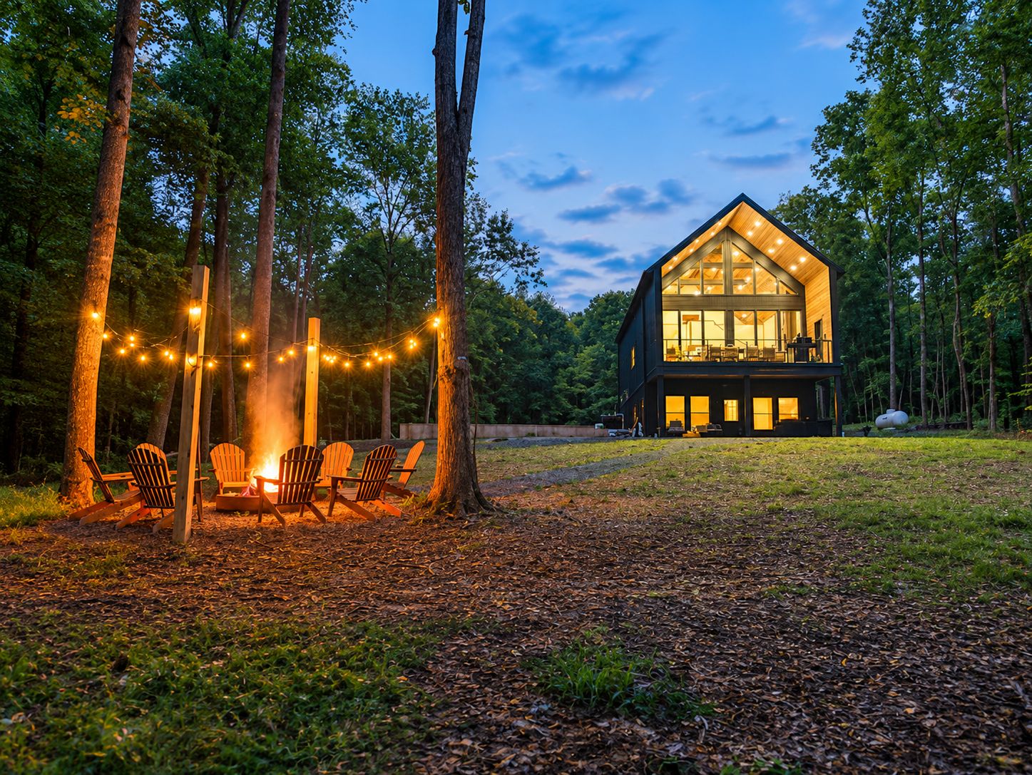 Une cabane dotée d’une grande façade vitrée, entourée d’arbres, et d’un foyer avec des sièges.