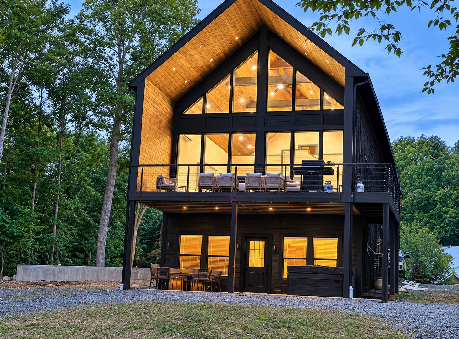 A two-story wooden cabin with large windows, a balcony, and outdoor seating.