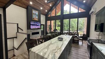A spacious kitchen with a marble island, large windows, and a TV displaying a sports event.