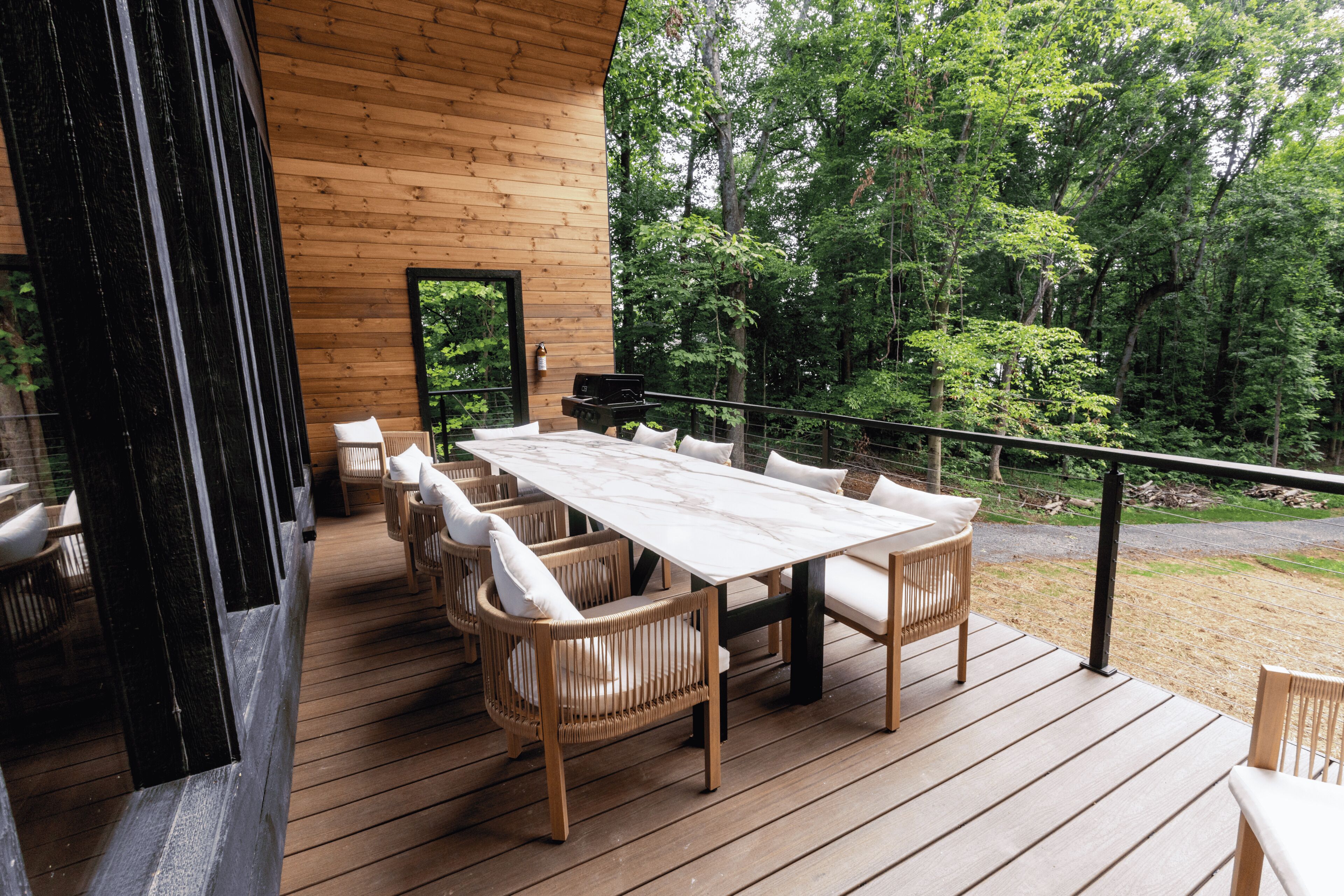 Una terraza de madera al aire libre con una mesa y sillas para comer, rodeada de un bosque.