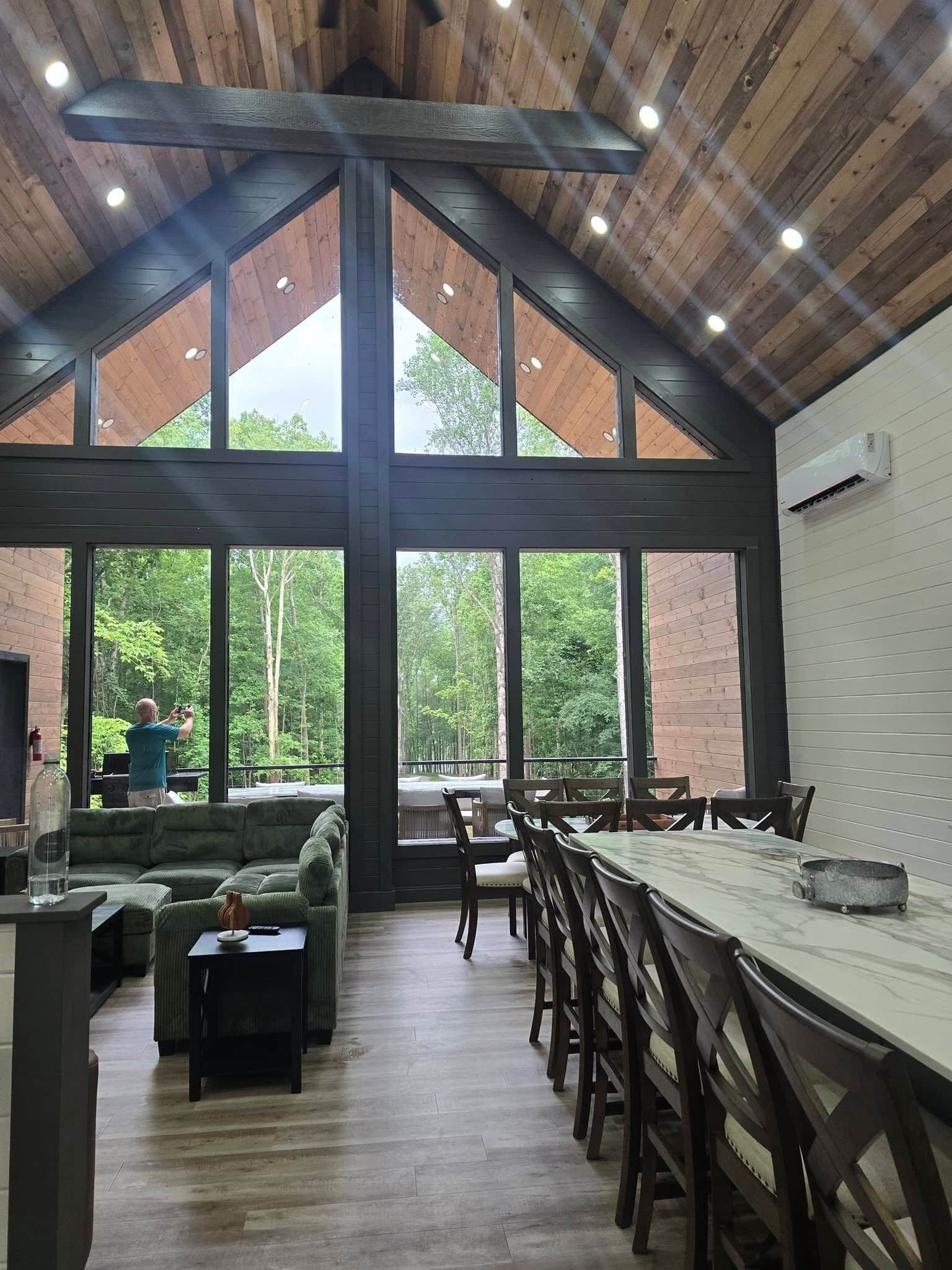 A spacious room with a high ceiling, large windows, a dining table, and a seating area.