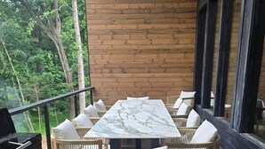 A wooden deck with a marble table and wicker chairs, surrounded by a wooden wall and large windows.