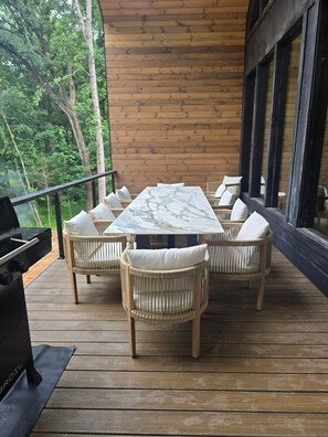 A wooden deck with a marble table and wicker chairs, surrounded by a wooden wall and large windows.
