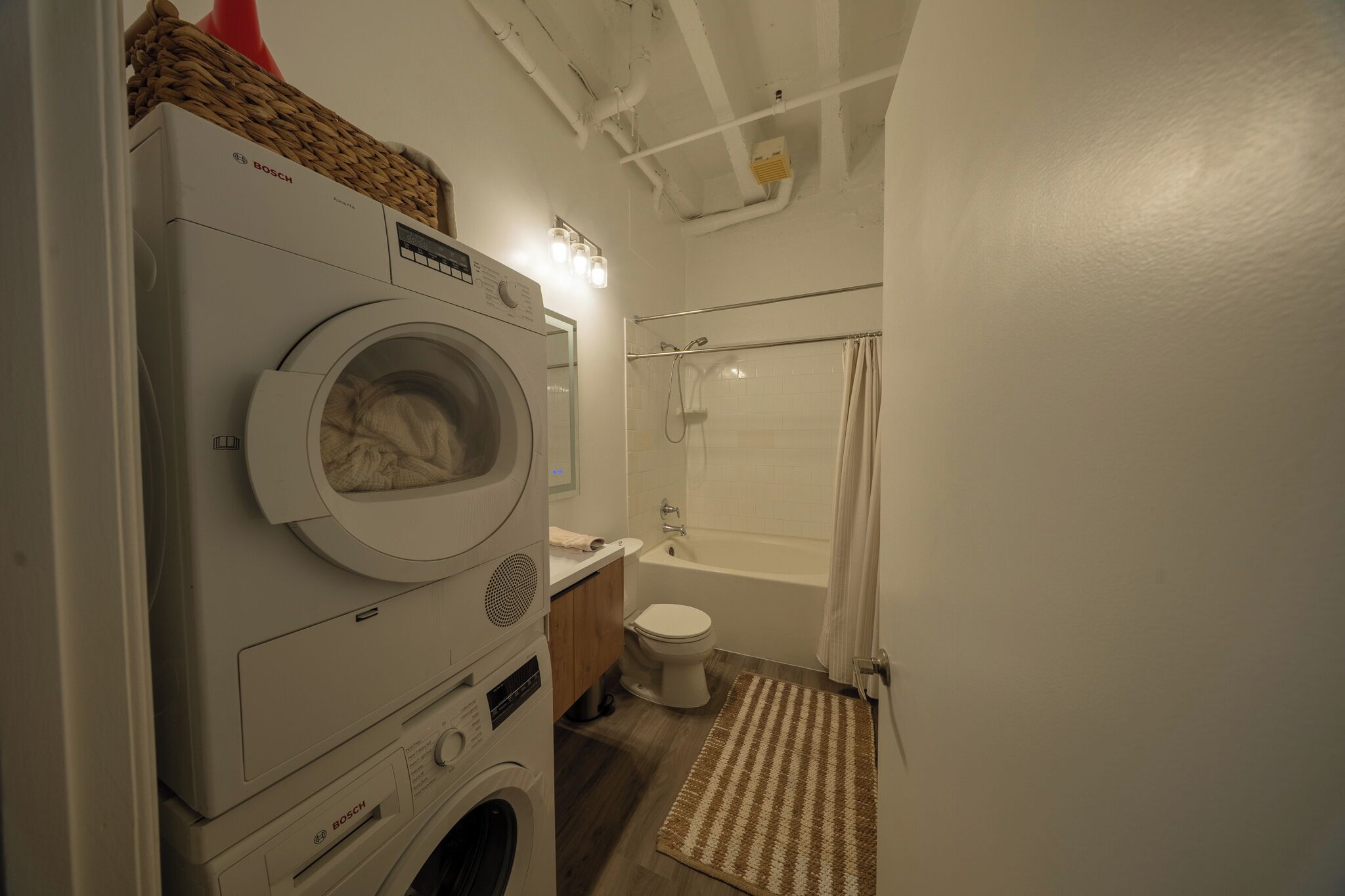 A compact bathroom with a front-loading washing machine, a toilet, and a shower area.