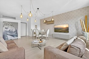 Ein modernes Wohnzimmer mit Essbereich, einer Couch, einem Couchtisch und einem an der Wand befestigten Fernseher.