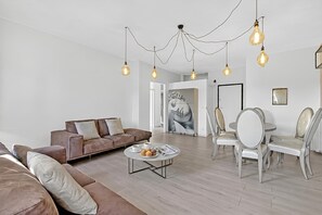 Ein modernes Wohnzimmer mit einer braunen Couch, einem runden Couchtisch mit Gebäck und einem Essbereich mit weißen Stühlen.