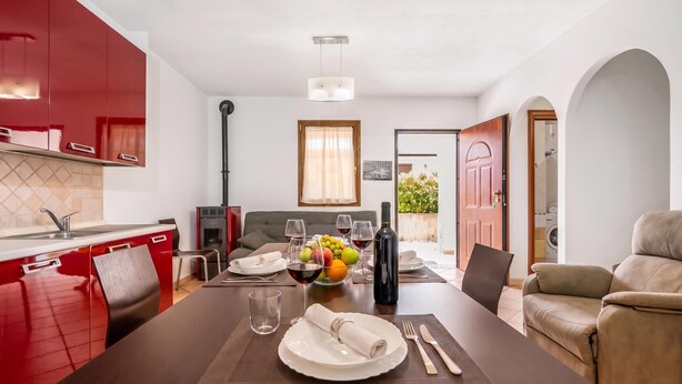 A modern kitchen with red cabinets, a dining area with a table set for two, and a view into the living room. - Budoni Beach Homes, Budoni, Italy (Budoni)