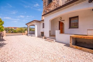 Eine moderne Villa mit Natursteinfassade, einer überdachten Terrasse und einer Zuwegung mit Kies.
