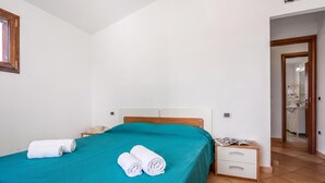 A bedroom with a bed, a nightstand, a mirror, and a door leading to a bathroom. - Budoni Beach Homes, Budoni, Italy (Budoni)