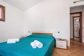 A bedroom with a bed, a nightstand, a mirror, and a door leading to a bathroom. - Budoni Beach Homes, Budoni, Italy (Budoni)