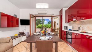 A modern kitchen with red cabinets, a dining area with a table set for two, and a TV mounted on the wall. - Budoni Beach Homes, Budoni, Italy (Budoni)