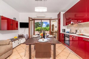 A modern kitchen with red cabinets, a dining area with a table set for two, and a TV mounted on the wall. - Budoni Beach Homes, Budoni, Italy (Budoni)