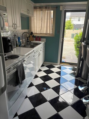 Une cuisine avec un sol à carreaux noirs et blancs, une fenêtre avec des rideaux et une vue sur l’extérieur.