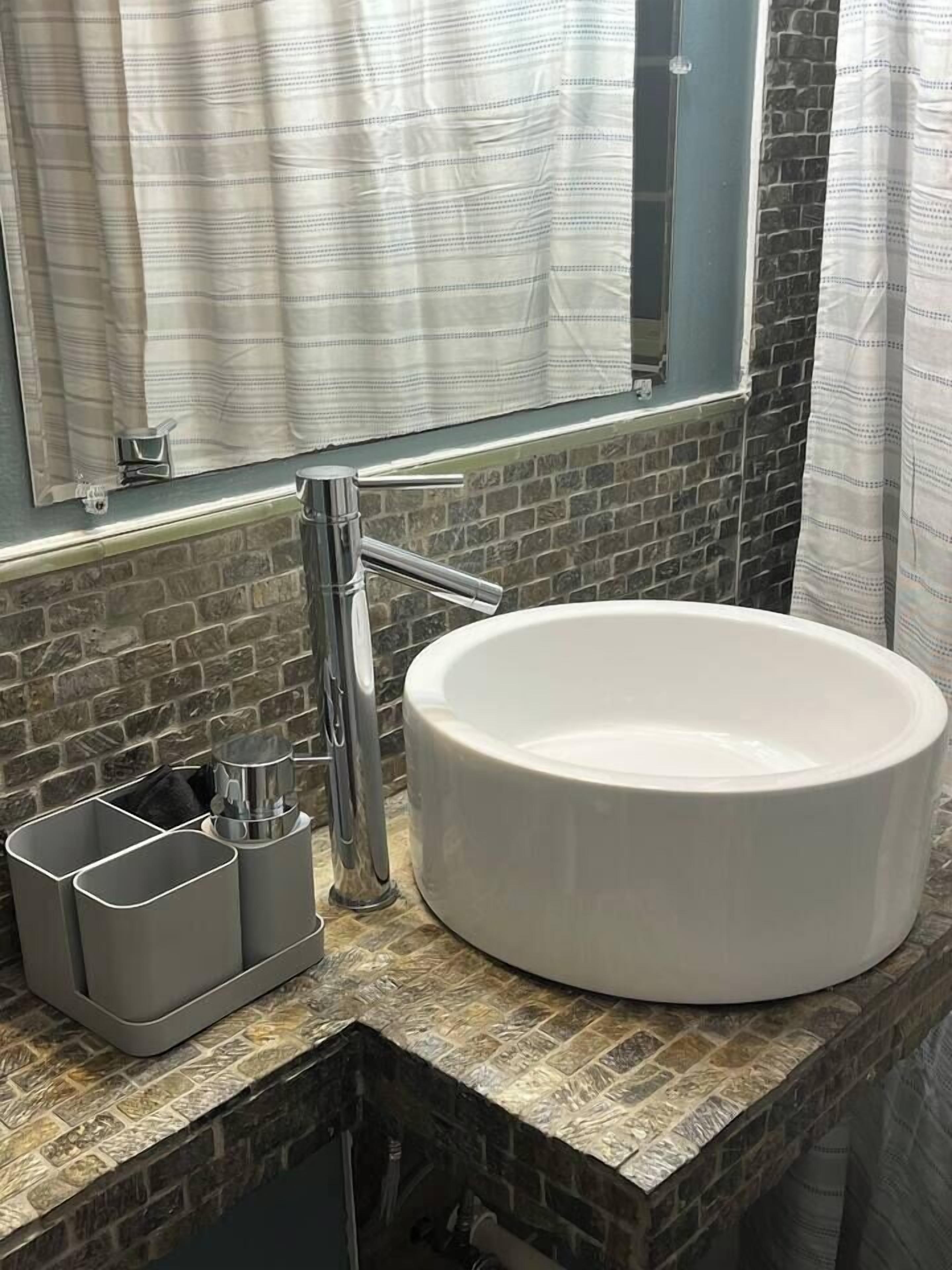 Une salle de bain avec un lavabo rond blanc, un robinet moderne et une fenêtre avec des rideaux.