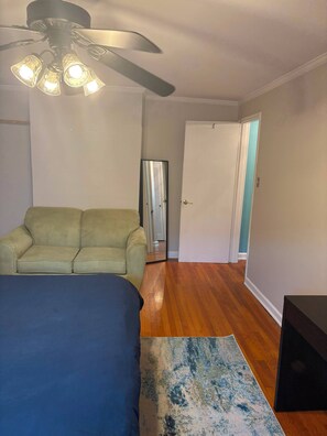 Une chambre à coucher avec un lit, un canapé vert, un ventilateur de plafond et une porte donnant sur une autre pièce.