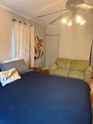 Ein Schlafzimmer mit einem Bett, einem grünen Sessel, einem Deckenventilator und einem Bild an der Wand.