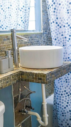 Une salle de bain avec un lavabo rond blanc, un robinet chromé et un rideau de douche à motifs pois bleus.