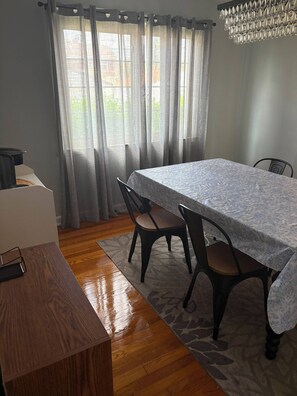 A dining area with a table, chairs, a chandelier, and a view through sheer curtains. - 2BR Condo by Airport and Downtown Cbus (Columbus)