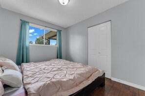 A bedroom with a bed, a window with curtains, a door, and a ceiling light. - Spacious Main-Floor Bungalow | Sleeps 6 | Near South Common & Southgate Mall (Edmonton)