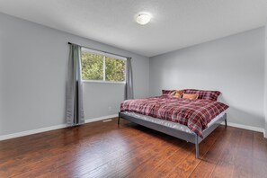 Een slaapkamer met een enkel bed, een raam met gordijnen en een plafondlamp.