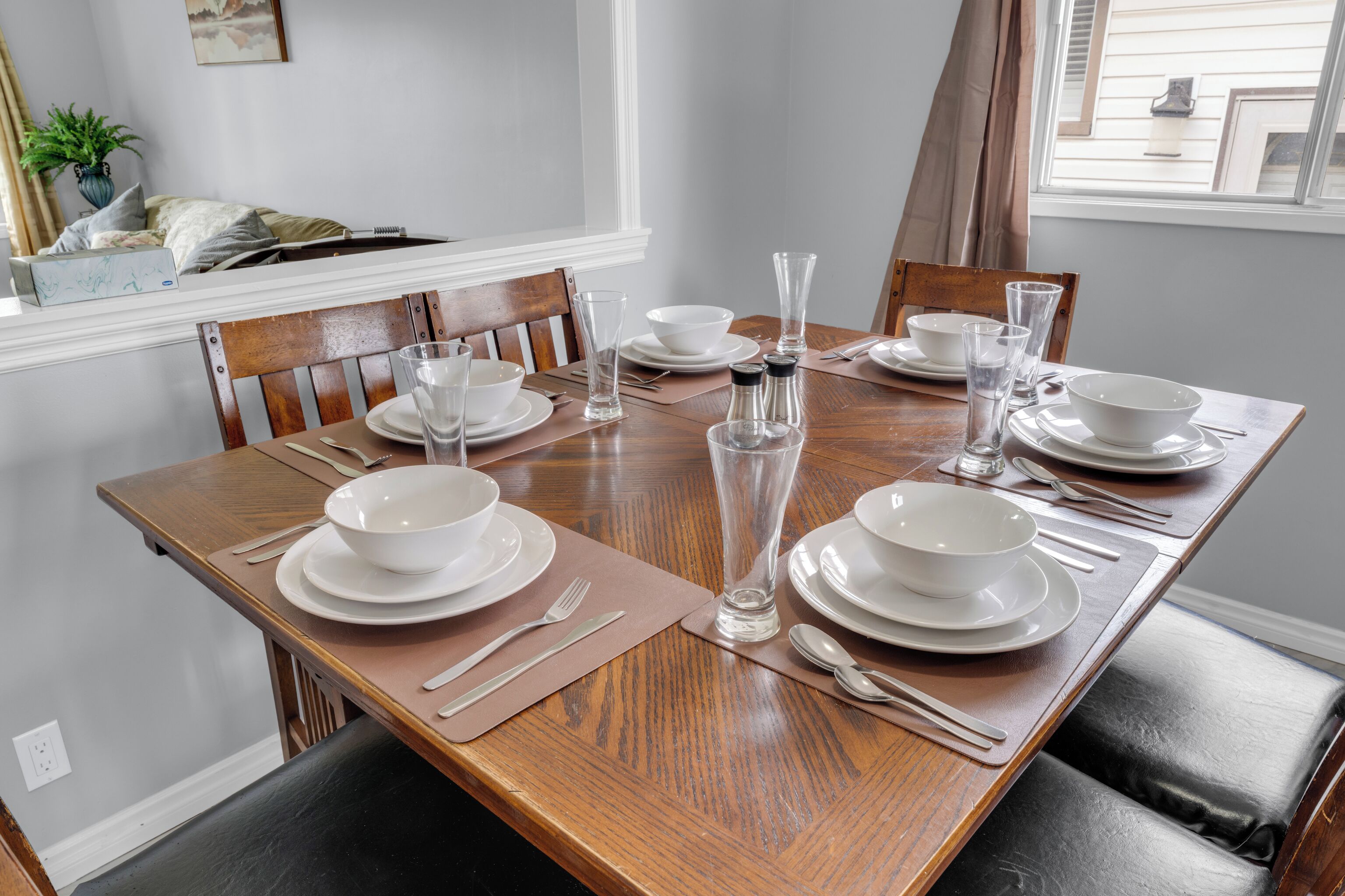 A dining table set with white plates, bowls, and clear glassware, surrounded by wooden chairs.
