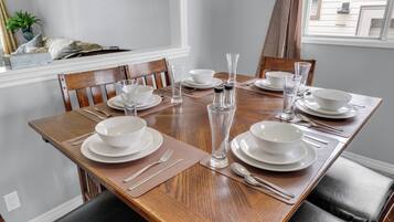 A dining table set with white plates, bowls, and clear glassware, surrounded by wooden chairs.