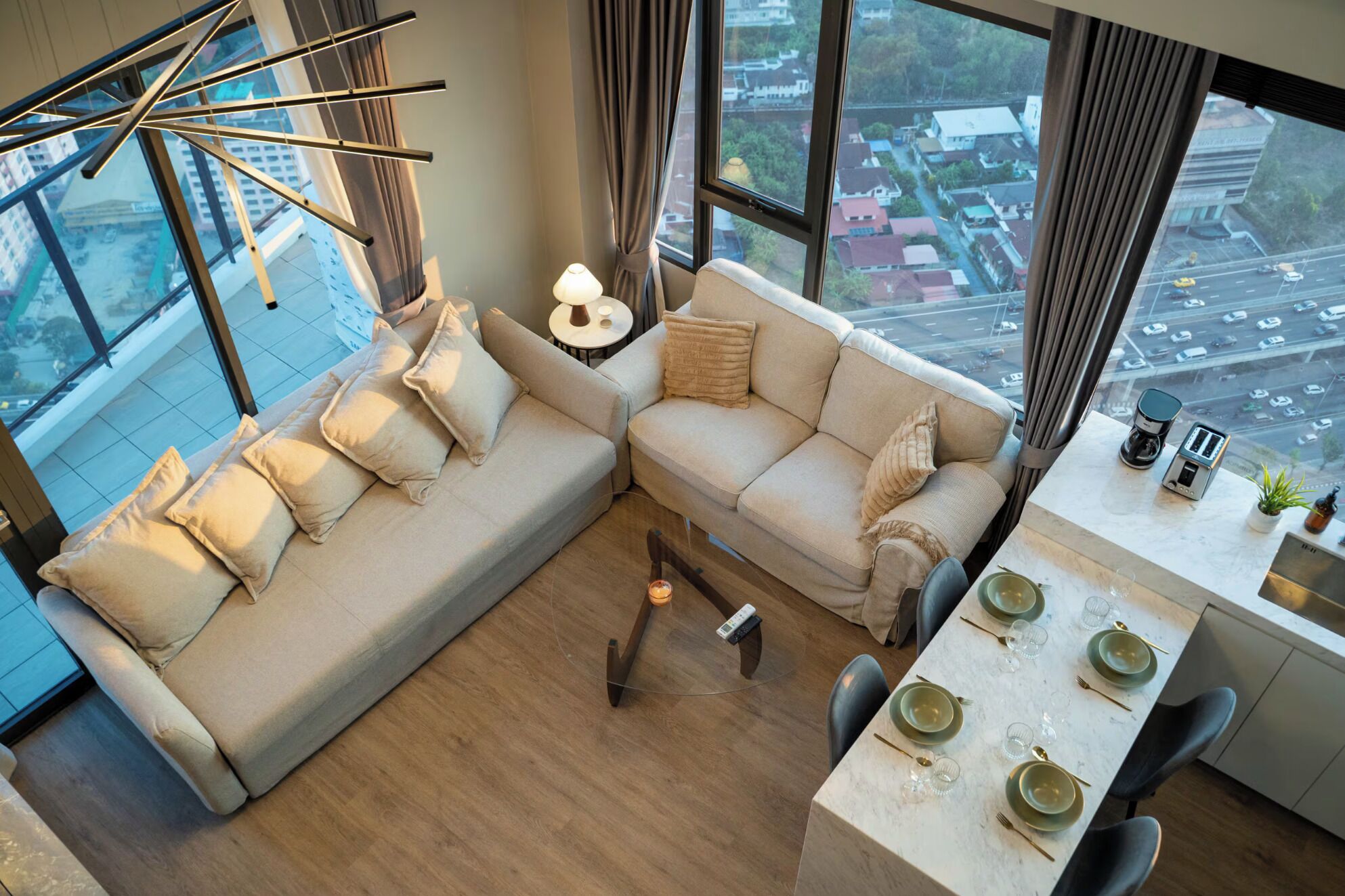 A modern living room with a sectional sofa, a dining table set for four, and a large window offering a city view.