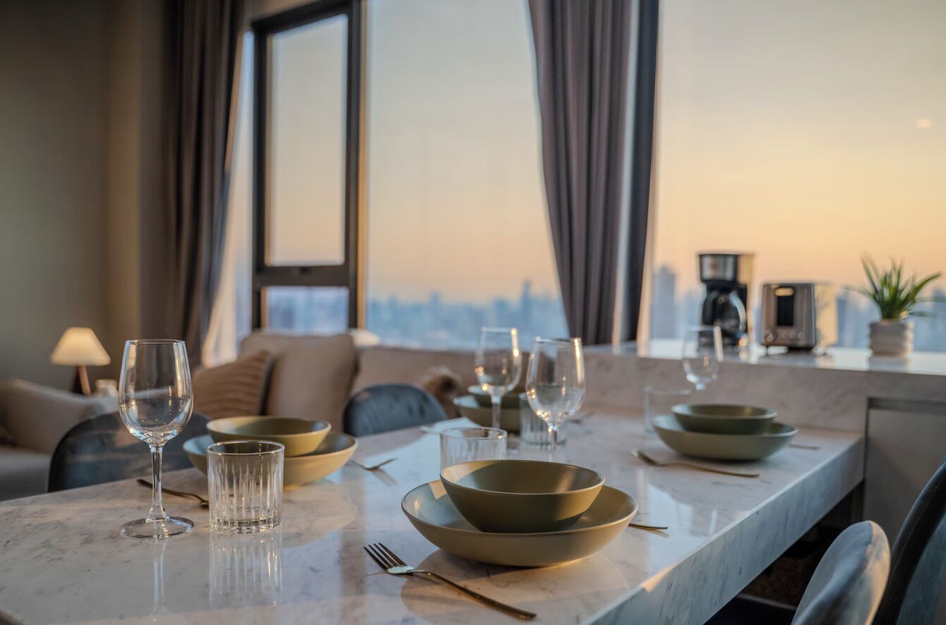 A dining table set with bowls, glasses, and cutlery in a modern interior with a city view.
