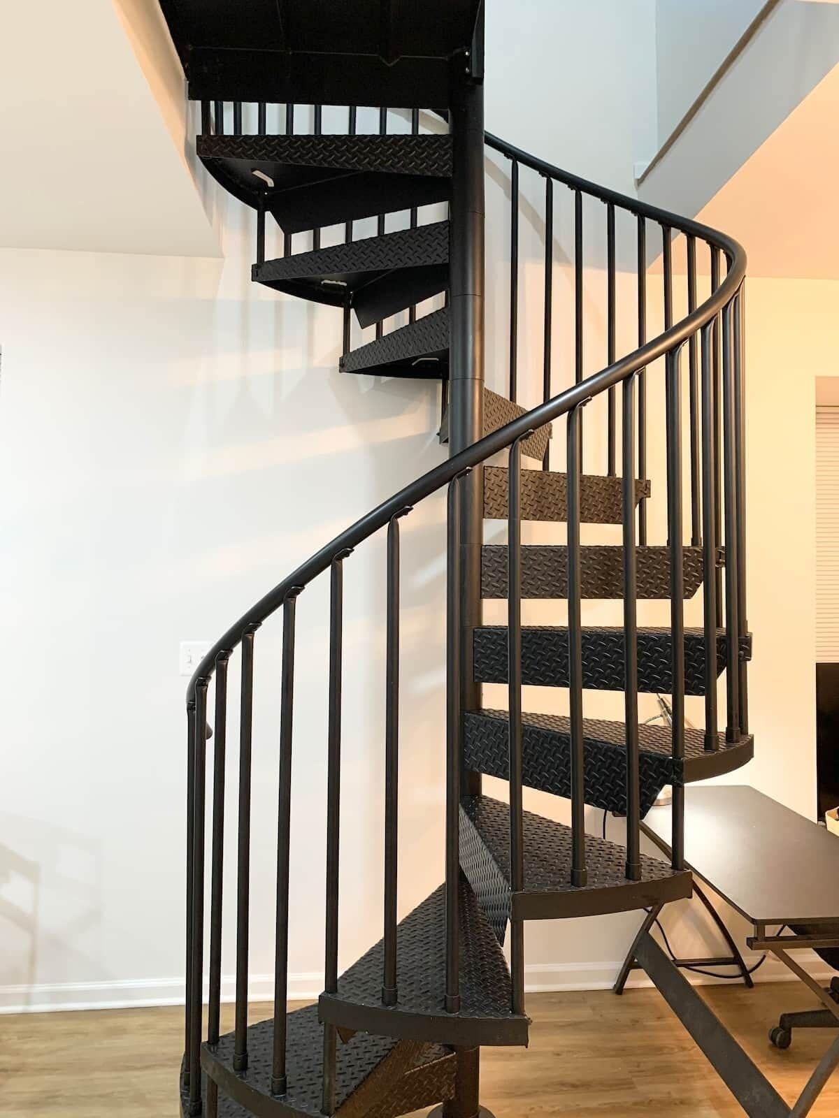 Un escalier en colimaçon avec une rampe en métal et des marches à surface texturée.