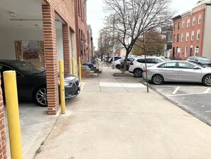 Ein Parkplatz mit Autos, die entlang eines Backsteinhauses und eines Gehwegs stehen, mit einem Baum im Hintergrund.
