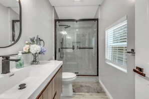 Een moderne badkamer met een wit wastafelmeubel, een douchecabine van glas en een toilet.