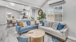 A modern living room with a blue sofa, a beige sofa, and a round coffee table. There is a dining area with a table and chairs, and a kitchen in the background. - Cozy Blue Cottage Near Old Town Monrovia, City of Hope. Pet-Friendly (Monrovia)