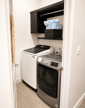 A compact laundry area with a washing machine and dryer, a small shelf above the dryer, and a door with a handle. - Sun City Oasis w/Heated Pool & Spa in El Paso (El Paso)