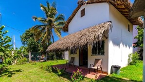 A white building with a thatched roof, a small porch with chairs, and a palm tree in the background. - Cabaña Paraguitos (Brisas de Zicatela)
