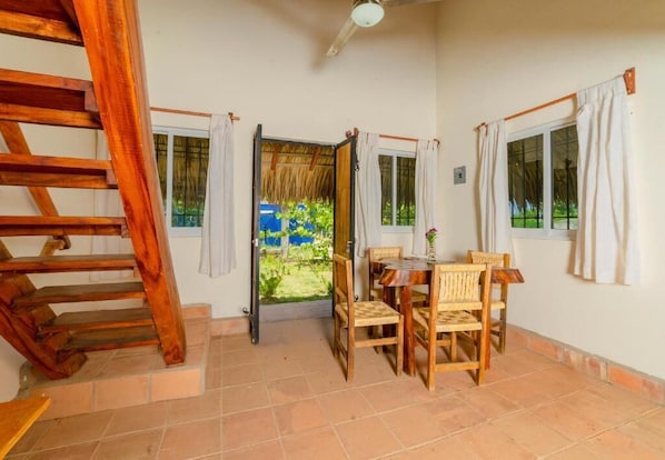 A room with a wooden staircase, a dining table with chairs, and a view of a garden through an open door. - Cabaña Paraguitos (Brisas de Zicatela)