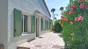 A building with a stone-paved entrance, green shutters, and a garden with pink flowers. - Villa l'Orangeraie by Interhome (Villeneuve-Loubet)