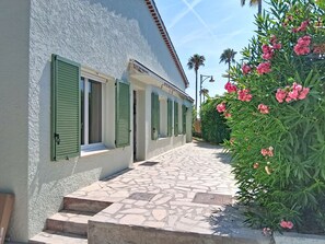 A building with a stone-paved entrance, green shutters, and a garden with pink flowers. - Villa l'Orangeraie by Interhome (Villeneuve-Loubet)