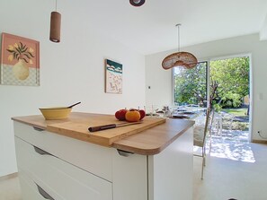 A modern kitchen with a wooden countertop, white cabinets, and a view of the outdoors through a glass door. - Villa l'Orangeraie by Interhome (Villeneuve-Loubet)