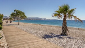 A pebble beach with a wooden walkway, palm trees, and a clear blue sea. - Villa l'Orangeraie by Interhome (Villeneuve-Loubet)