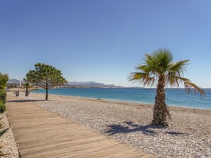 A pebble beach with a wooden walkway, palm trees, and a clear blue sea. - Villa l'Orangeraie by Interhome (Villeneuve-Loubet)