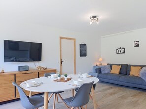 Ein modernes Wohnzimmer mit Essbereich, einem Flachbildfernseher, einer Couch und Wandbildern.